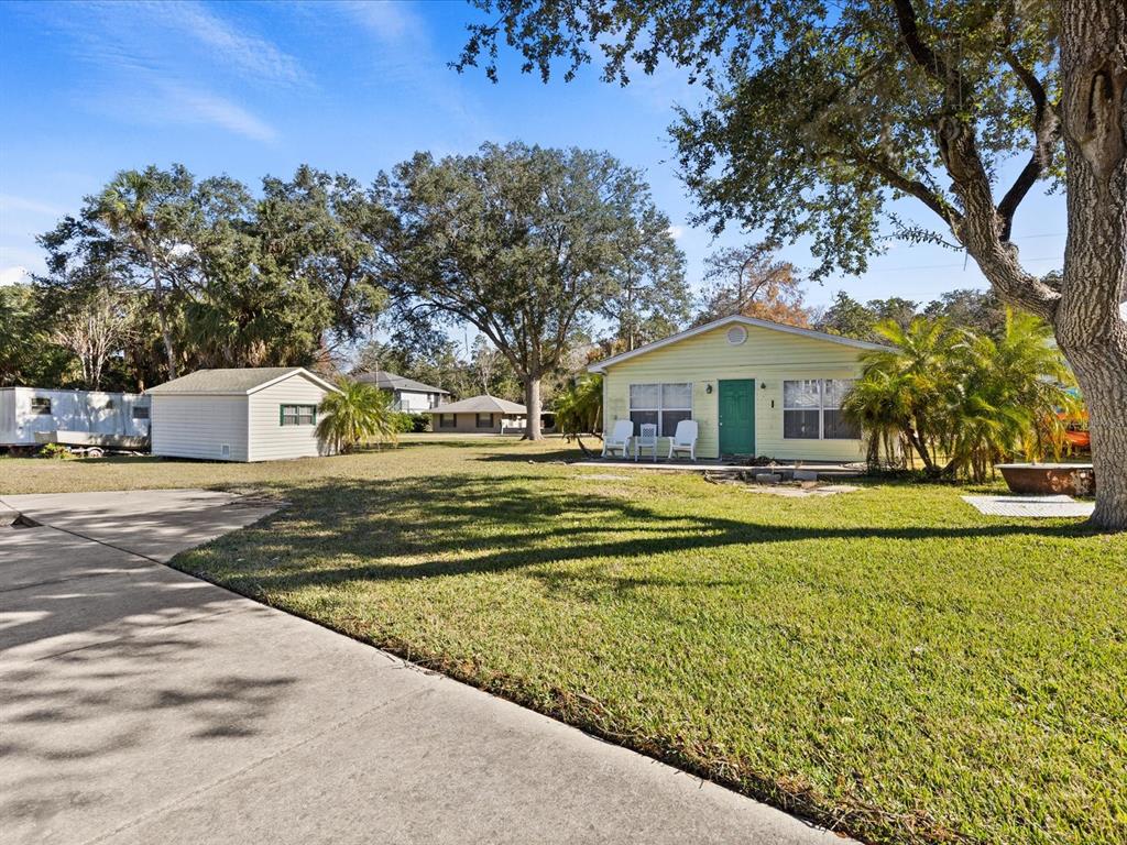 A yellow house with a green door sits on a grassy lot with a shed — 7255 TROPICAL DRIVE, WEEKI WACHEE, FL