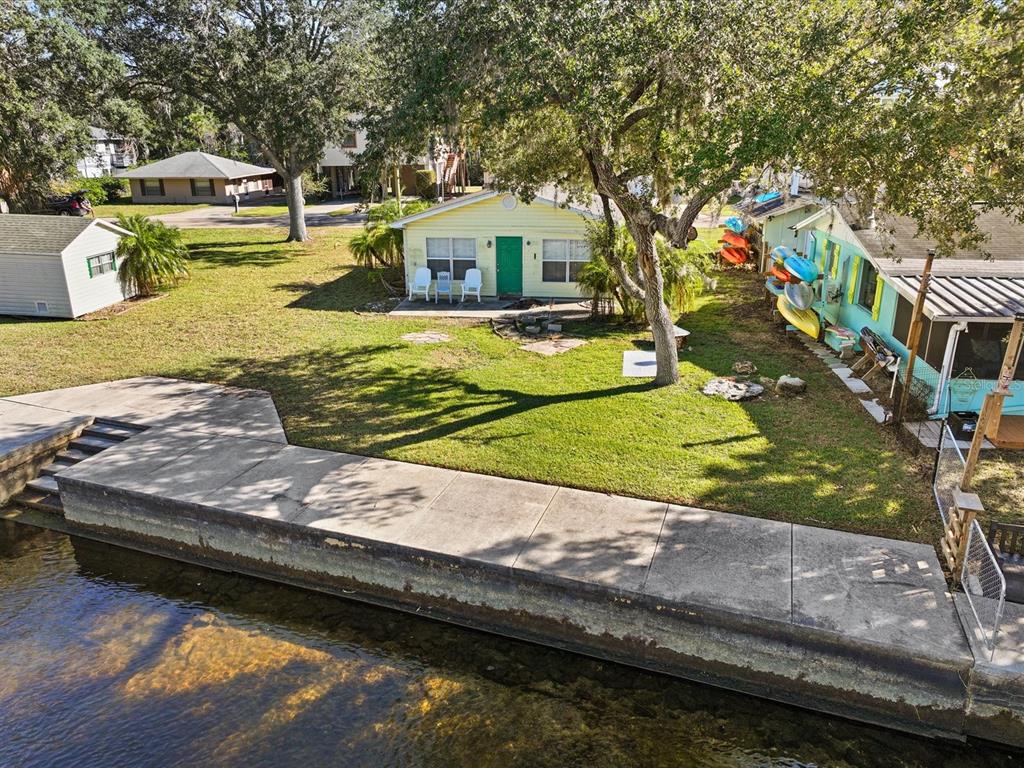 An aerial view shows a waterfront property with a yellow cottage, lawn, and concrete bulkhead — 7255 TROPICAL DRIVE, WEEKI WACHEE, FL