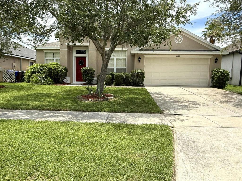 A single-story suburban house with a tan exterior, red front door, and a two-car garage — 3539 MAPLE RIDGE LOOP, KISSIMMEE, FL