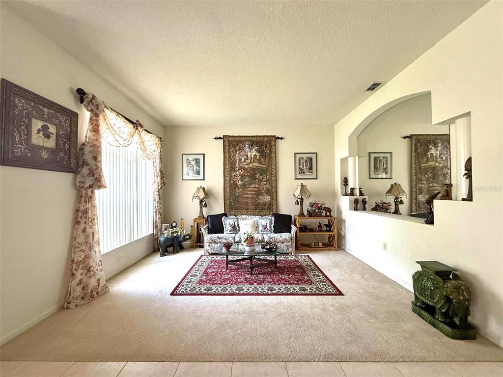 A living room features beige carpeting, a floral sofa, a red area rug, and wall art — 3539 MAPLE RIDGE LOOP, KISSIMMEE, FL