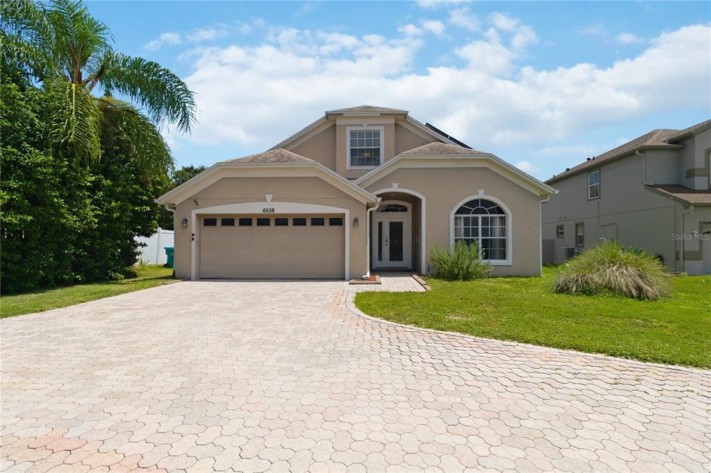 A tan single-story house features a two-car garage and a paved driveway under a blue sky — 6658 LAKE PEMBROKE PLACE, ORLANDO, FL