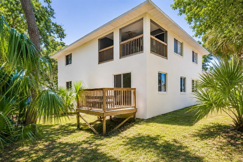 A two-story house with a wooden deck, screened-in upper balcony, and surrounding palm trees — 601 E 2ND AVENUE, NEW SMYRNA BEACH, FL