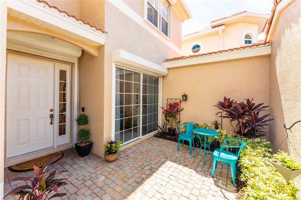A paved courtyard features a white front door, sliding glass doors, and turquoise patio furniture — 3341 SUNSET KEY CIRCLE, PUNTA GORDA, FL