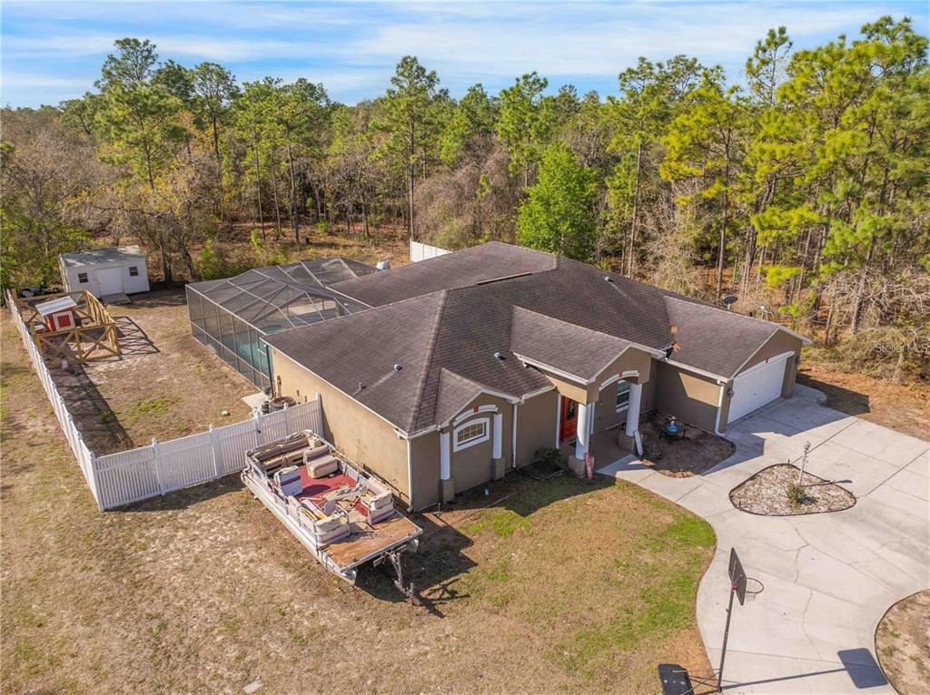 An aerial view of a tan house with a pool enclosure, driveway, and parked pontoon boat — 13040 QUIGLEY AVENUE, WEEKI WACHEE, FL
