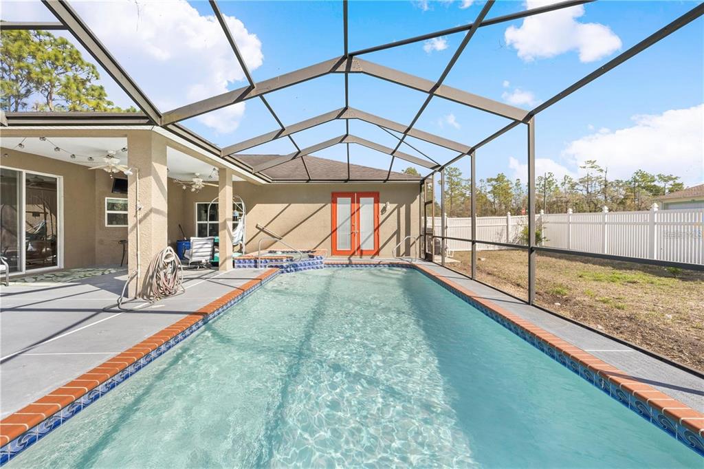 A swimming pool with a brick border sits inside a screened-in lanai with a patio — 13040 QUIGLEY AVENUE, WEEKI WACHEE, FL