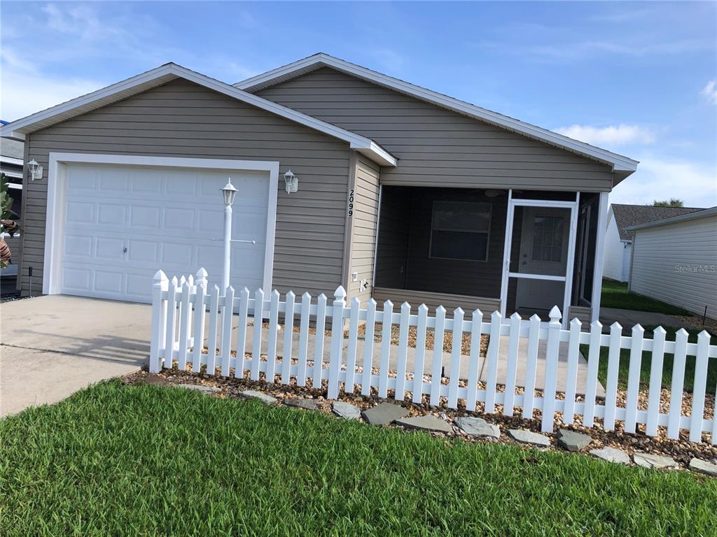 A single-story house with tan siding, a white garage door, and a white picket fence — 2099 BROYHILL AVENUE, THE VILLAGES, FL