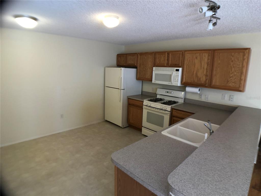 A kitchen with wood cabinets, white appliances, and a gray countertop peninsula — 2099 BROYHILL AVENUE, THE VILLAGES, FL