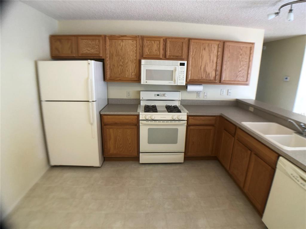 A kitchen with oak cabinets, white appliances, and light-colored countertops — 2099 BROYHILL AVENUE, THE VILLAGES, FL