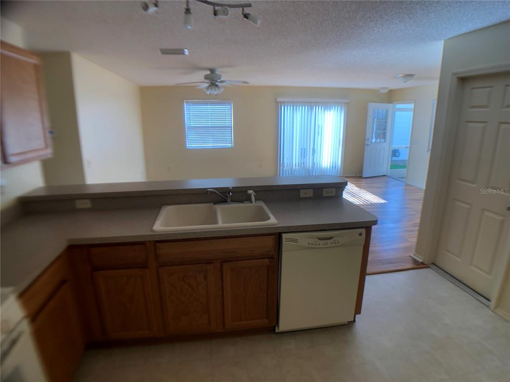 A kitchen with wood cabinets and a white dishwasher overlooks a living area with flooring — 2099 BROYHILL AVENUE, THE VILLAGES, FL