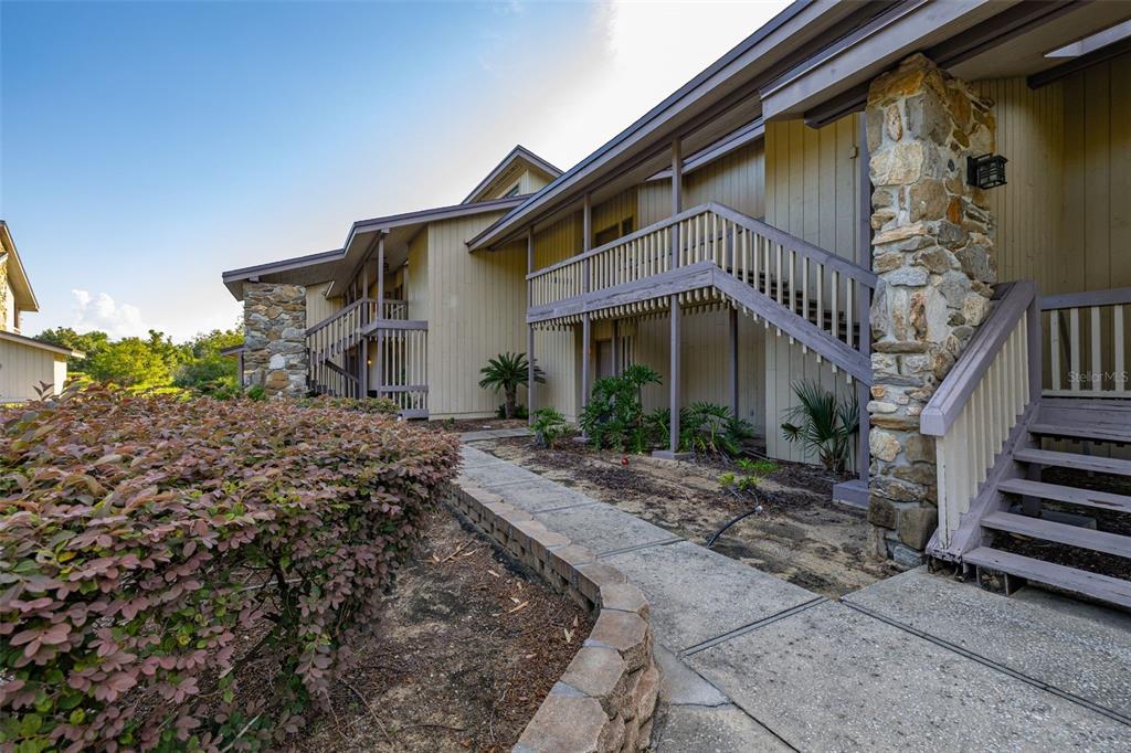 A two-story apartment building exterior features tan siding, stone pillars, and wooden staircases — 2272 BURNWAY ROAD UNIT 2272, HAINES CITY, FL