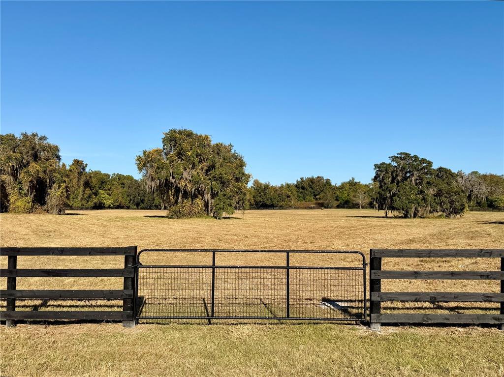 A black metal gate and wooden fence enclose a large, dry, grassy field with trees — 0 SE 116TH PLACE, OCALA, FL