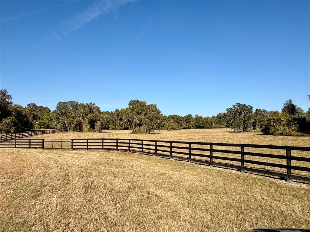 A black wooden fence encloses a large, dry grassy field under a clear blue sky — 0 SE 116TH PLACE, OCALA, FL
