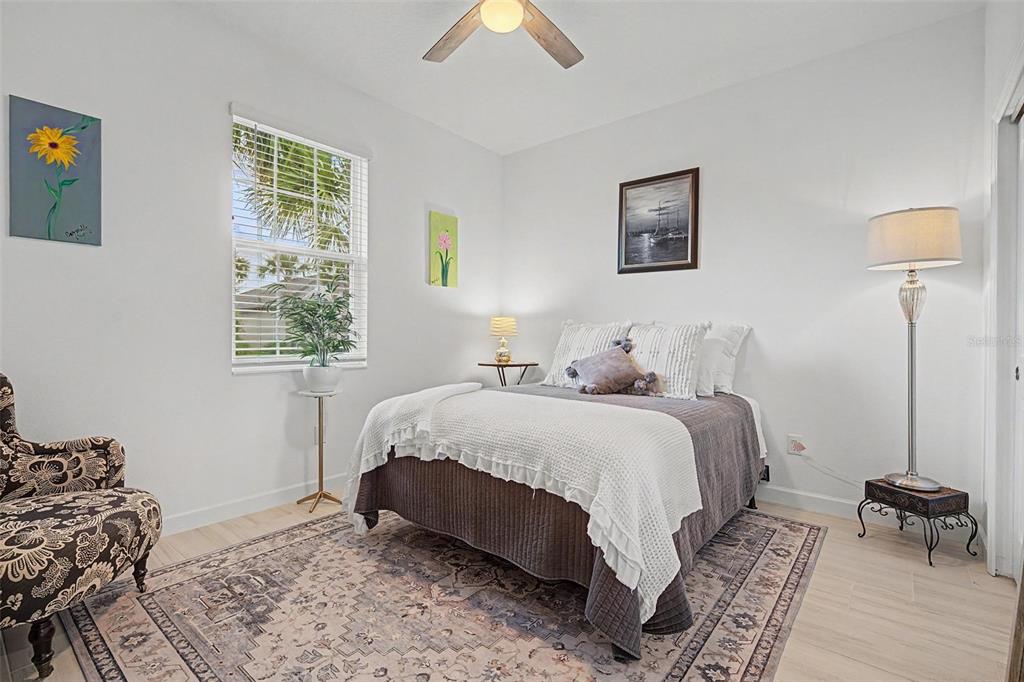 A bedroom features a bed, patterned armchair, area rug, and wall art under a ceiling fan — 10499 GABLE DIG LOOP, SAN ANTONIO, FL