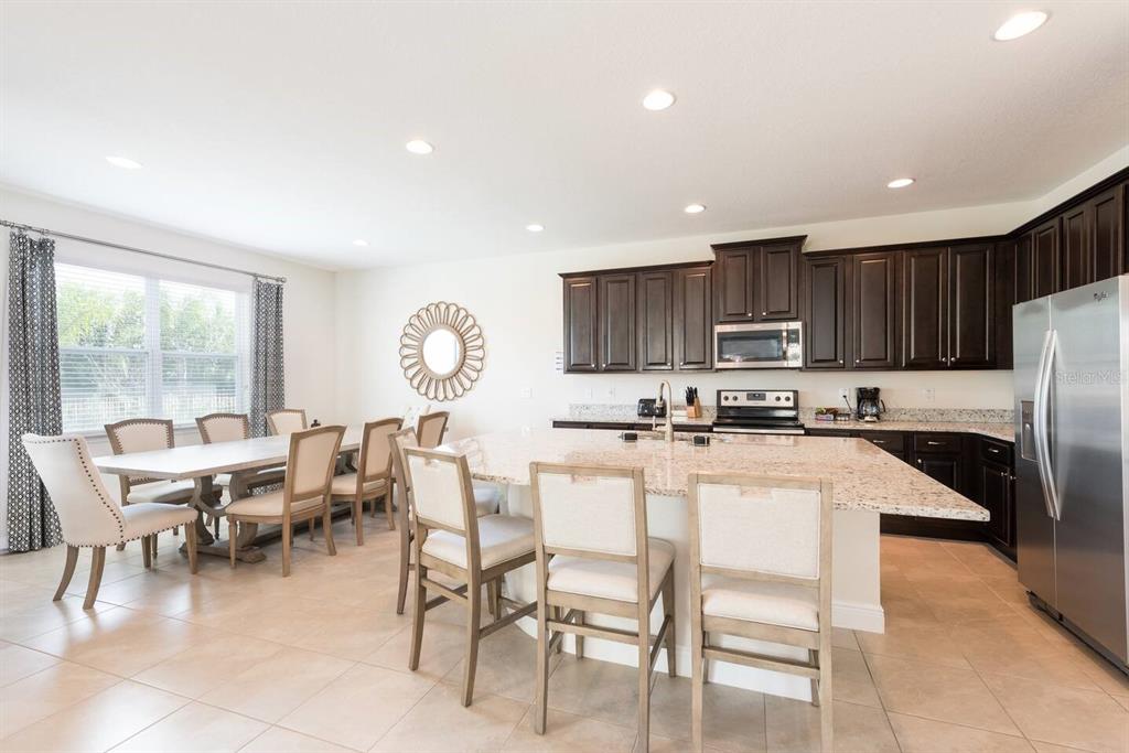 A kitchen and dining area with dark wood cabinets, granite countertops, and light tile flooring — 7467 MARKER AVE, KISSIMMEE, FL