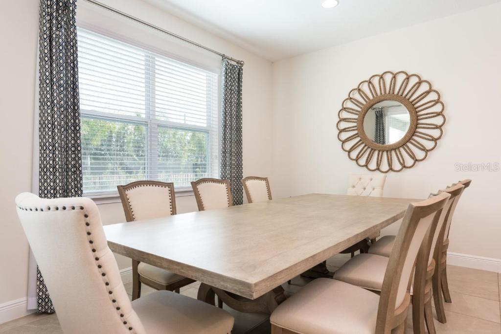 A dining room features a light wood table, upholstered chairs, and a large sunburst mirror — 7467 MARKER AVE, KISSIMMEE, FL
