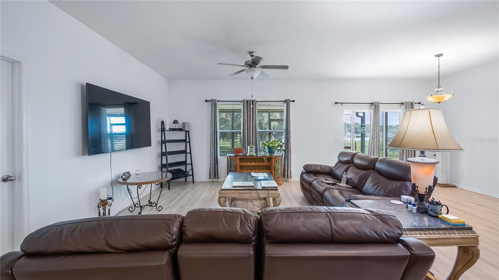 A living room features a large brown leather sofa, a television, and a ceiling fan — 15409 IVORY GULL LANE, MASCOTTE, FL