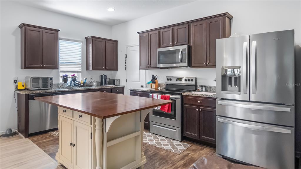 A kitchen features dark wood cabinets, stainless steel appliances, and a central wooden island — 15409 IVORY GULL LANE, MASCOTTE, FL