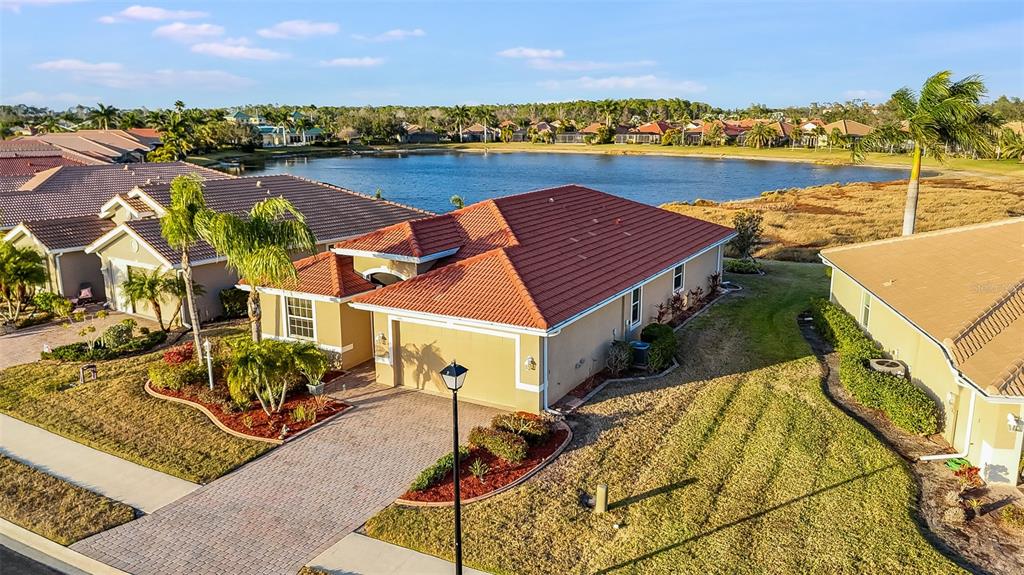 An aerial view shows a tan house with a red tile roof near a lake — 7486 TALON BAY DRIVE, NORTH PORT, FL