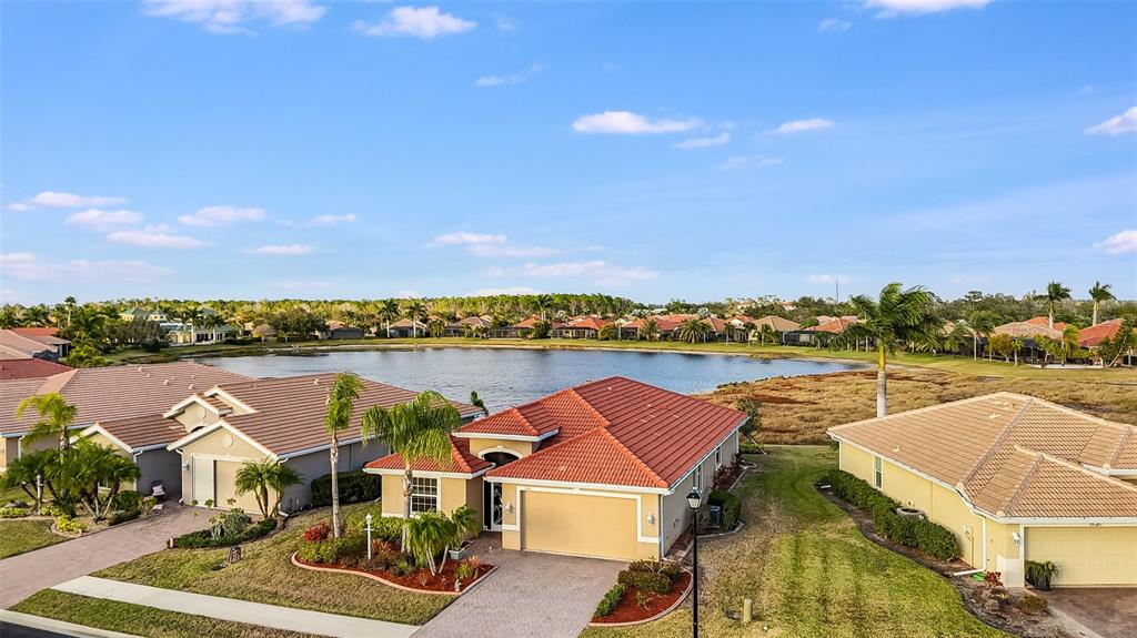 An aerial view shows suburban houses with tiled roofs surrounding a central lake — 7486 TALON BAY DRIVE, NORTH PORT, FL