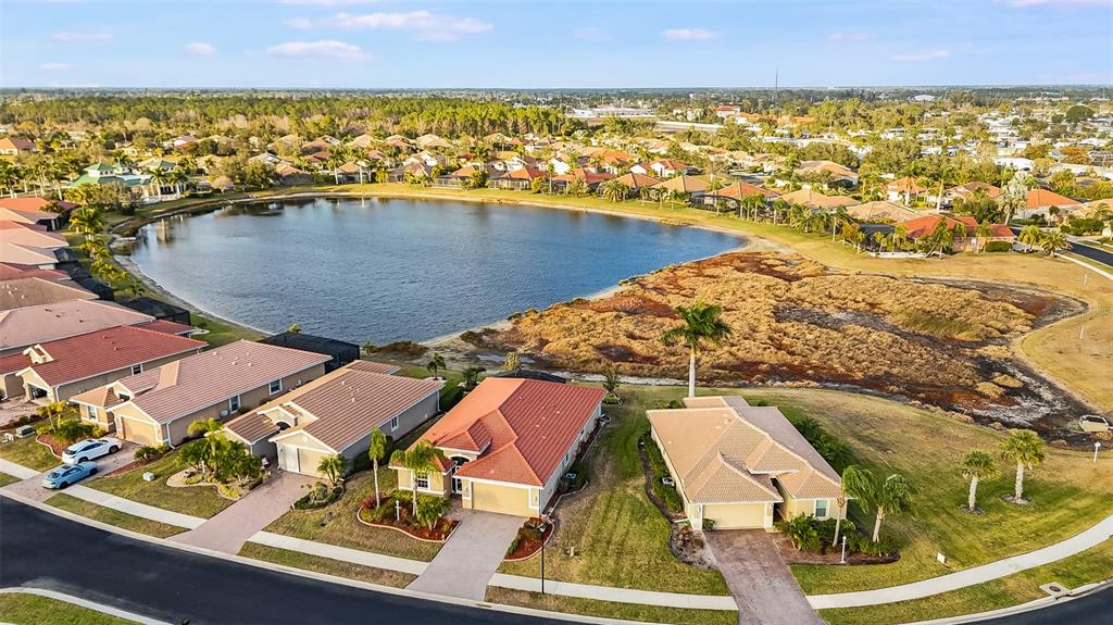 An aerial view shows suburban houses with tiled roofs situated along a lake and wetlands — 7486 TALON BAY DRIVE, NORTH PORT, FL