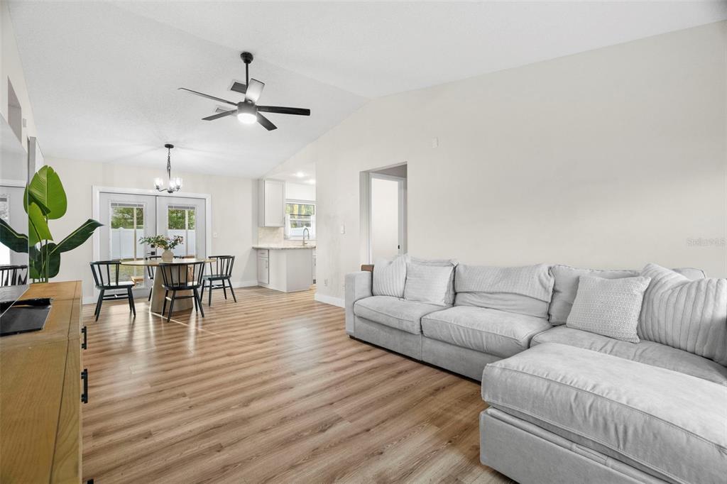 A living room with light wood-look flooring, a gray sectional sofa, and an adjacent dining area — 6500 BRIAR RIDGE COURT N, PINELLAS PARK, FL