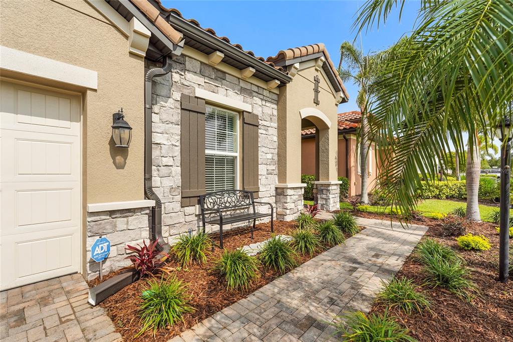 A stone-accented house exterior features a paved walkway, a small bench, and a palm tree — 2745 62ND AVENUE E, ELLENTON, FL