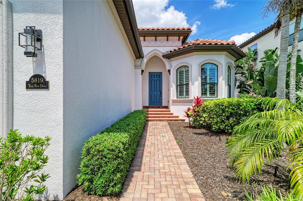 A brick walkway leads to the blue front door of a house with stucco walls — 5819 TITLE ROW DRIVE, BRADENTON, FL
