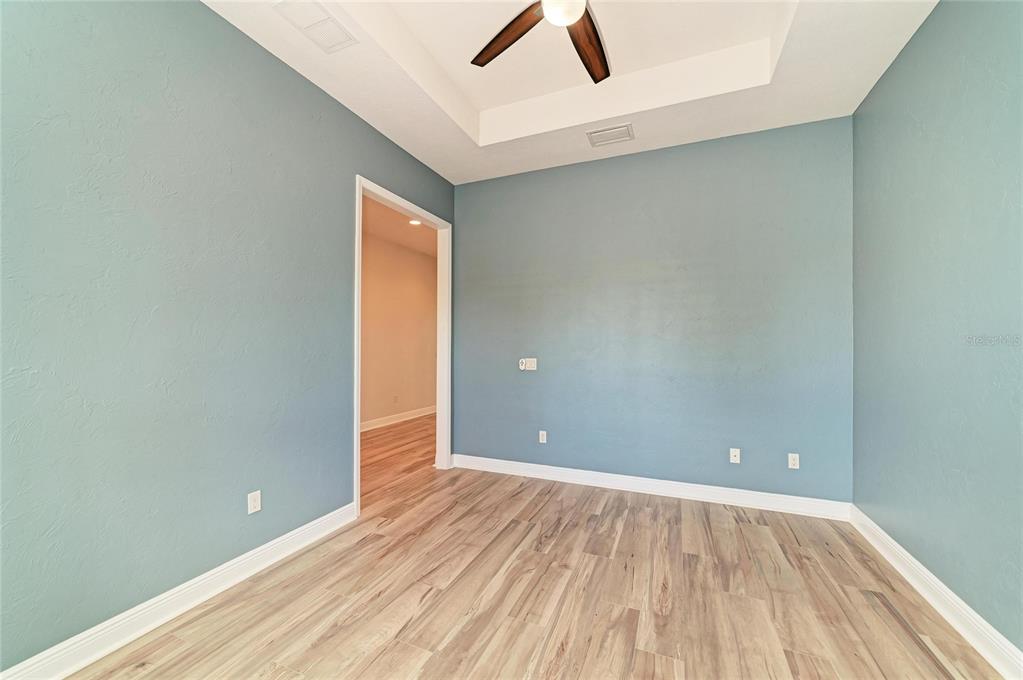An empty room with blue walls, light wood-look flooring, and a tray ceiling with a fan — 5819 TITLE ROW DRIVE, BRADENTON, FL