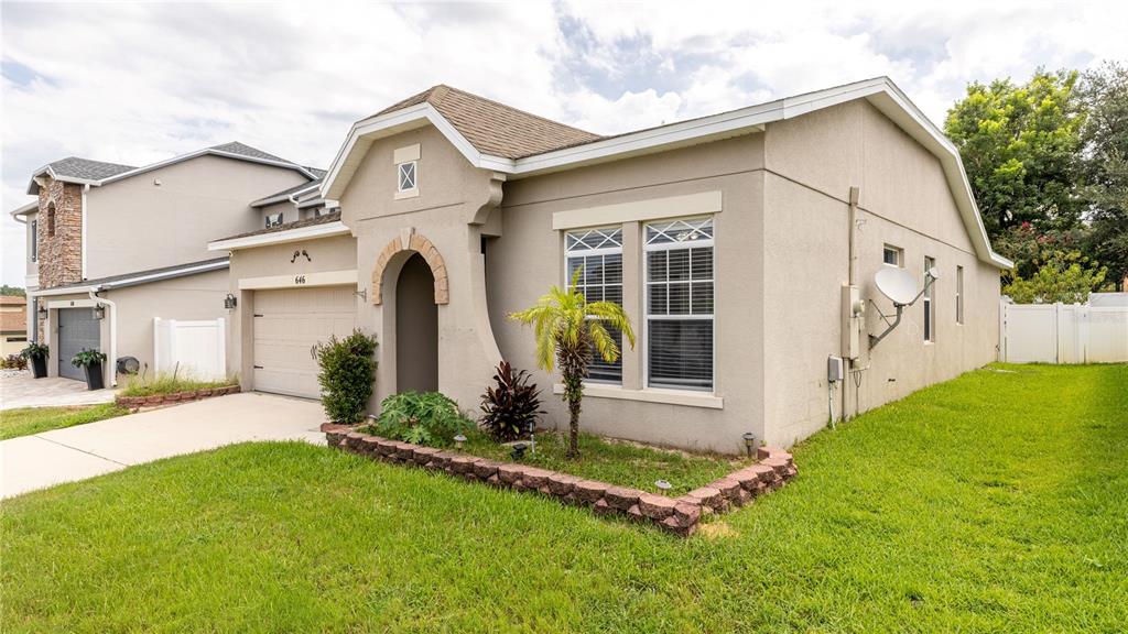 A single-story house with a tan stucco exterior, a small front garden, and a garage — 646 ARBOR POINTE AVENUE, MINNEOLA, FL