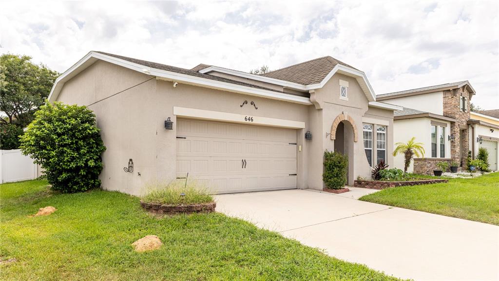 A beige, single-story house with a two-car garage and a small front yard — 646 ARBOR POINTE AVENUE, MINNEOLA, FL