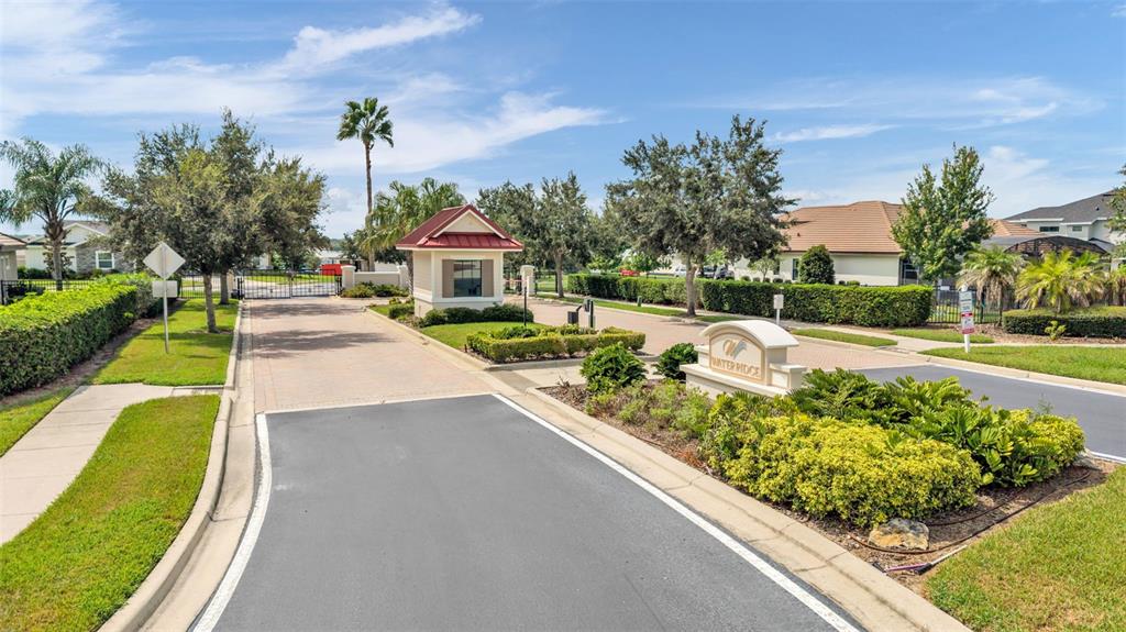 A gated entrance features a guardhouse, paved driveway, and landscaping under a blue sky — 534 BLUE FLAG DRIVE, AUBURNDALE, FL