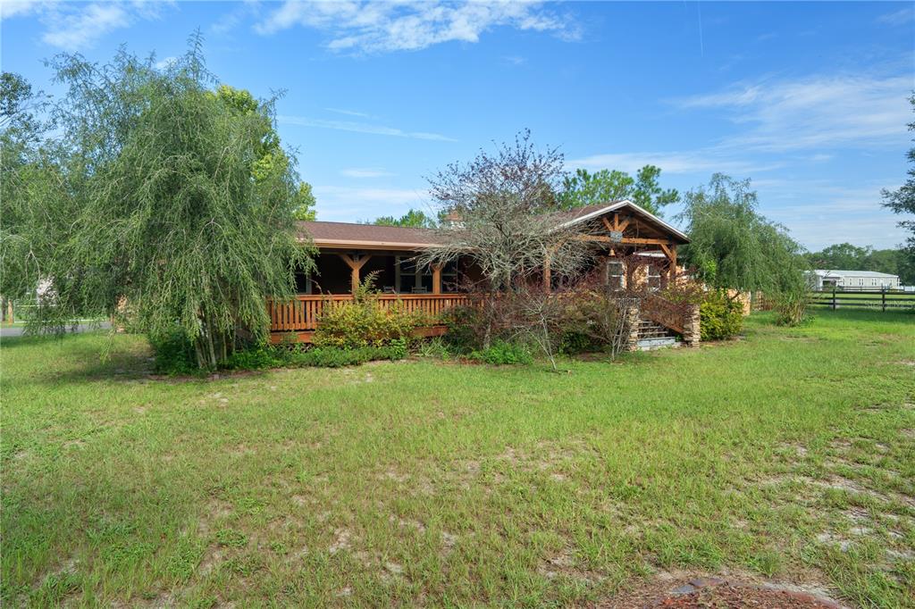 A single-story house with a large wooden porch and deck sits on a grassy lot — 4235 ALLEN ROAD, ZEPHYRHILLS, FL