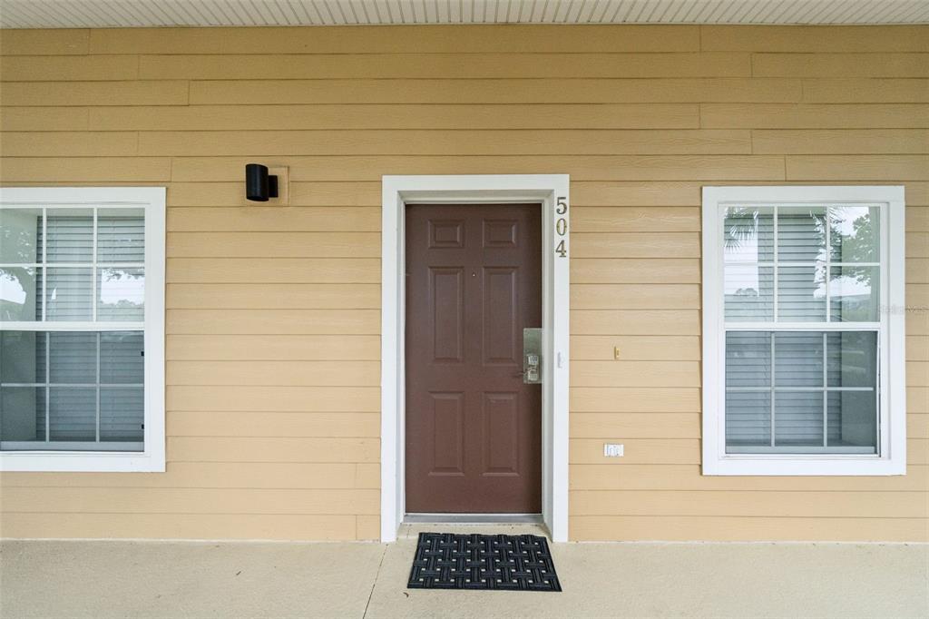 A brown front door with the number 504 is centered between two windows on beige siding — 504 RUM RUN, DAVENPORT, FL