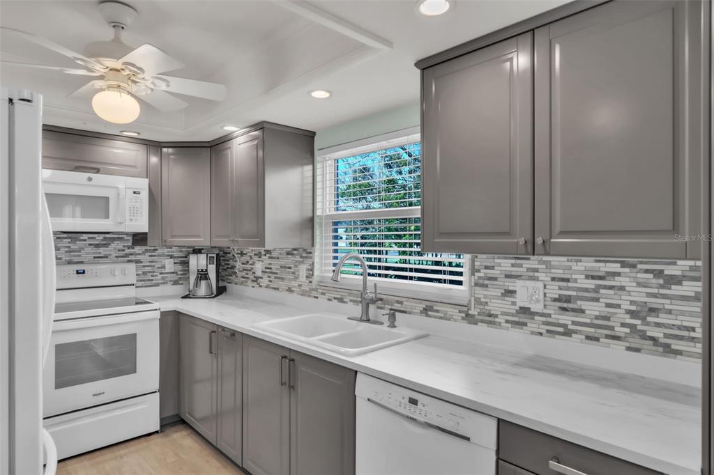 A kitchen with gray cabinets, white countertops, a white appliance suite, and a tiled backsplash — 600 MANATEE AVENUE UNIT 145, HOLMES BEACH, FL