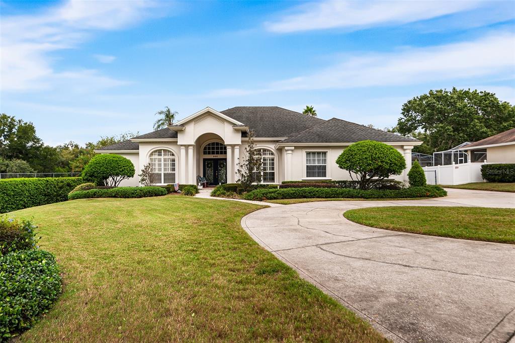 A single-story house with a curved concrete driveway and manicured landscaping under a blue sky — 902 HANOVER WAY, LAKELAND, FL