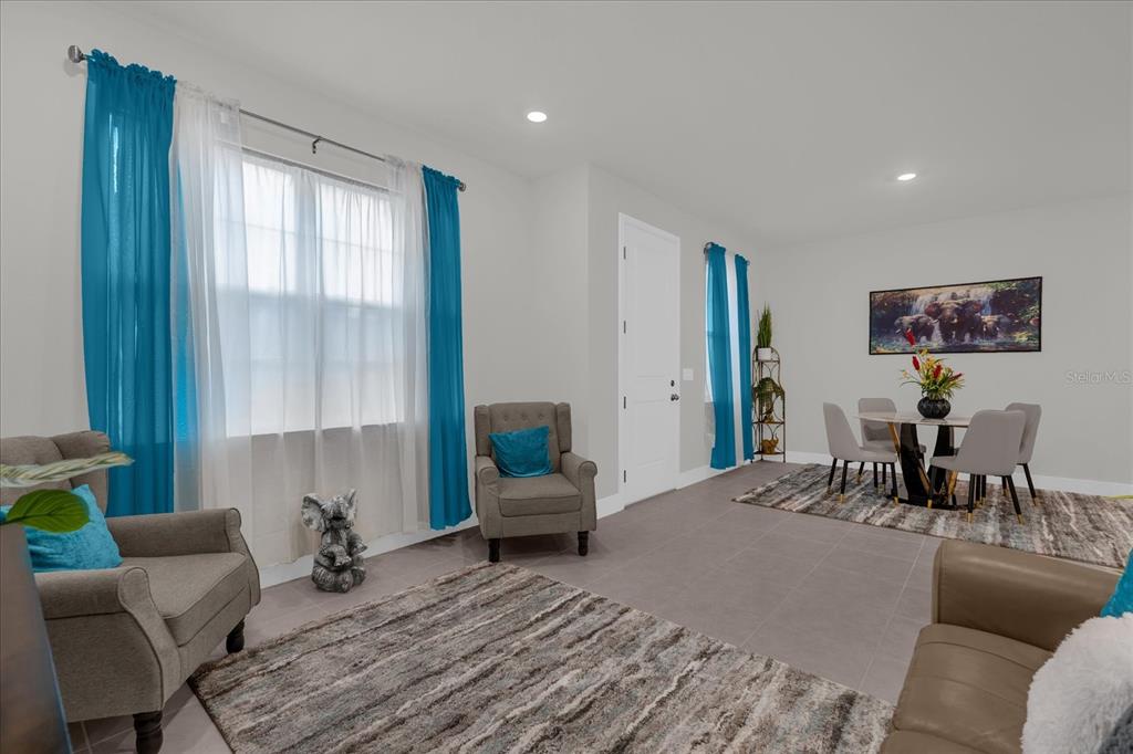 A living and dining area features gray tile floors, blue curtains, and neutral furniture — 3309 GRANDE HERON DRIVE, ST CLOUD, FL