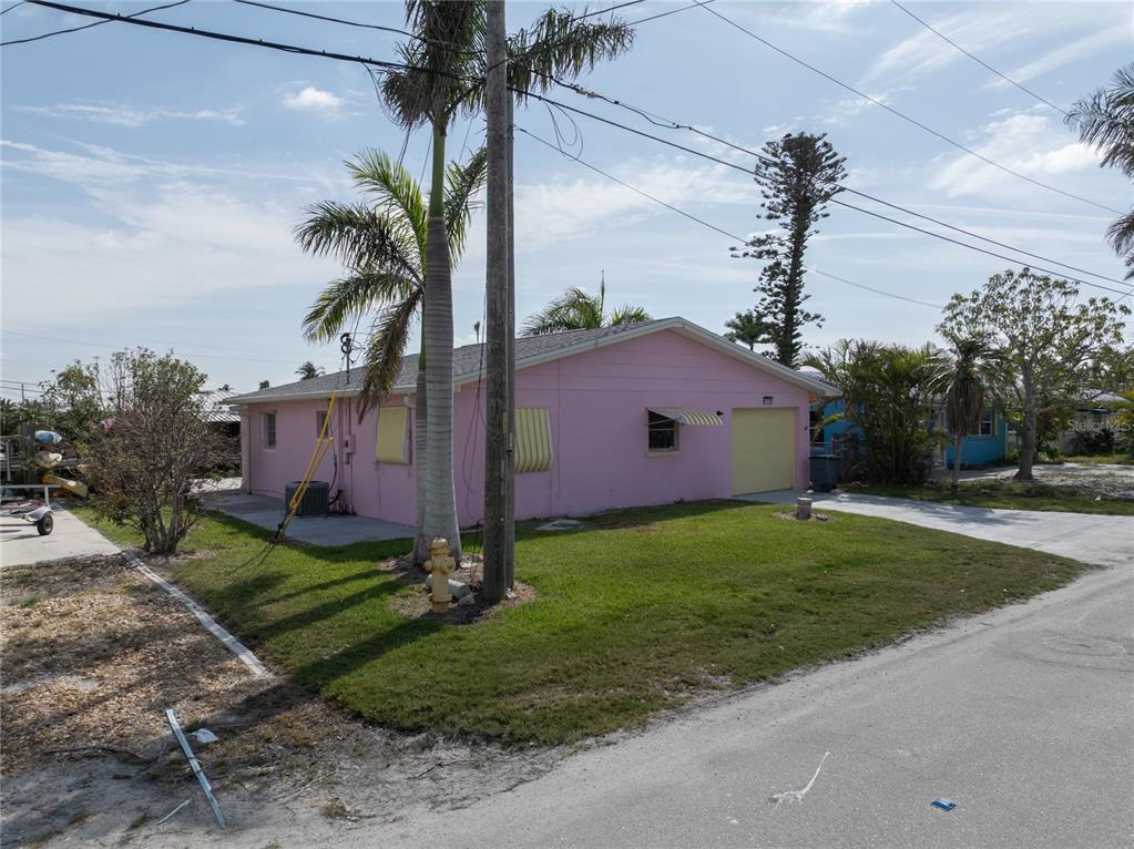 A pink, single-story house with a yellow garage door sits on a grassy corner lot — 11476 MAY STREET, MATLACHA, FL