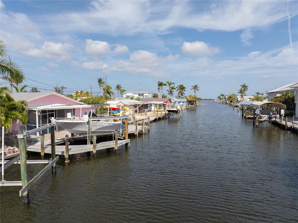 A canal lined with houses, boat docks, and palm trees under a blue sky — 11476 MAY STREET, MATLACHA, FL