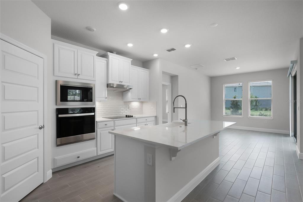 A modern kitchen features white cabinetry, stainless steel appliances, a quartz island, and tile flooring — 11899 SHINE VIEW LANE, WINTER GARDEN, FL