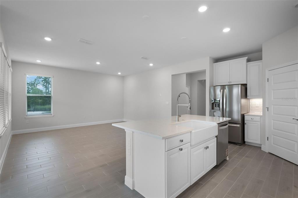 A kitchen island with a farmhouse sink sits in front of a spacious living area — 11899 SHINE VIEW LANE, WINTER GARDEN, FL
