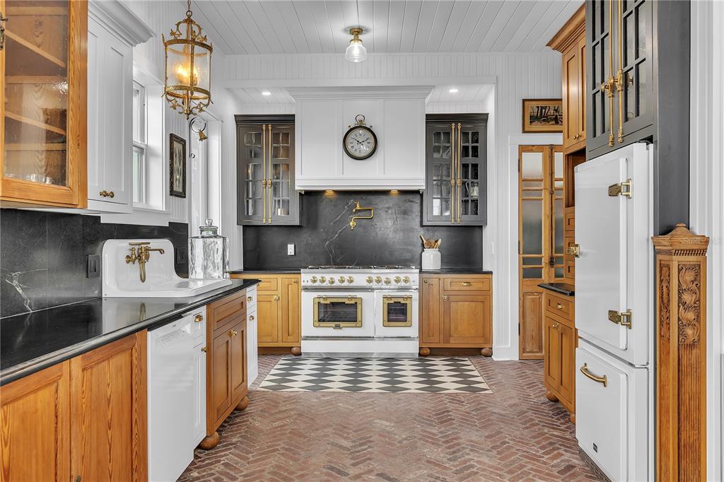 A kitchen features wood cabinets, black countertops, a white range, and a brick floor — 8241 MAIN STREET, BOKEELIA, FL