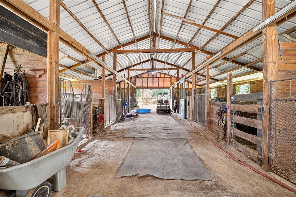 An interior view of a rustic horse barn with stalls, dirt flooring, and metal roofing — 10195 NW 160TH STREET, REDDICK, FL