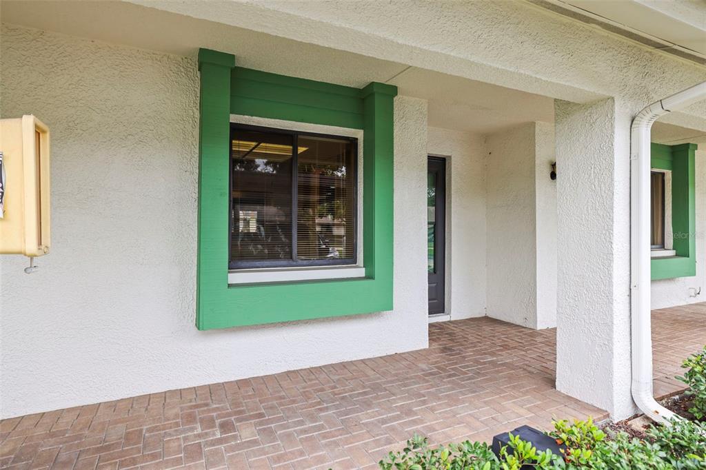 A covered entryway features a brick-paved porch, white stucco walls, and green-trimmed windows — 2556 ROYAL PINES CIRCLE UNIT 13-C, CLEARWATER, FL