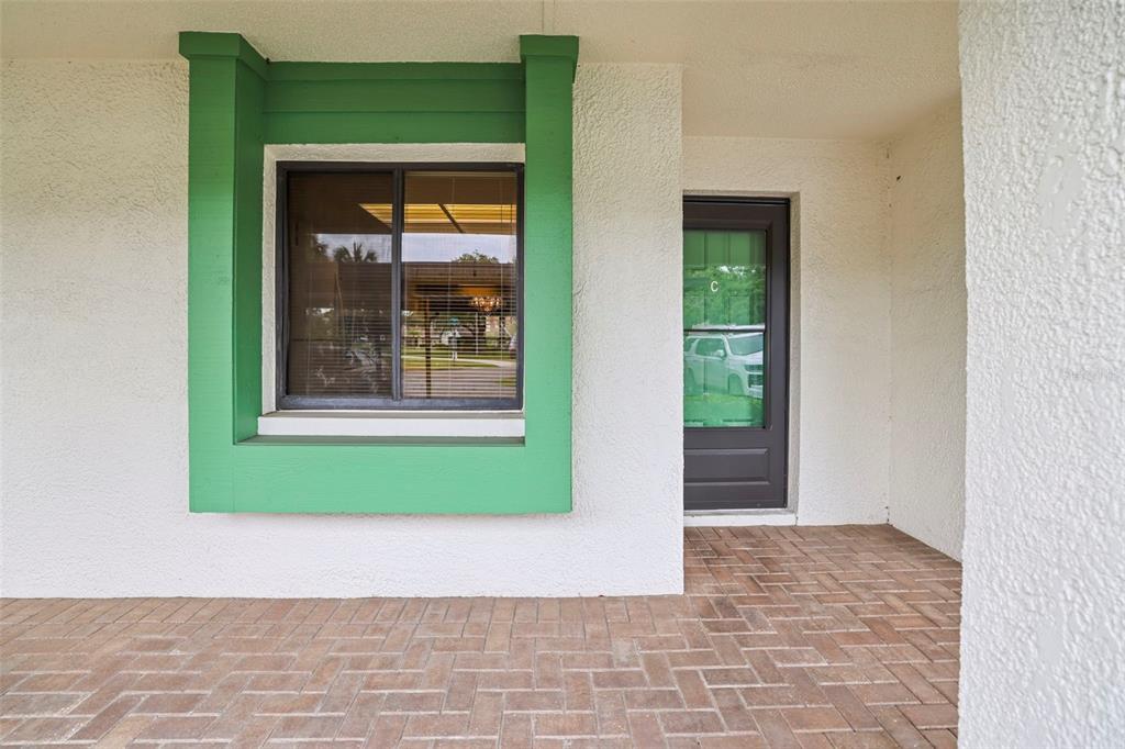 A brick patio leads to a dark door and a window framed in bright green — 2556 ROYAL PINES CIRCLE UNIT 13-C, CLEARWATER, FL