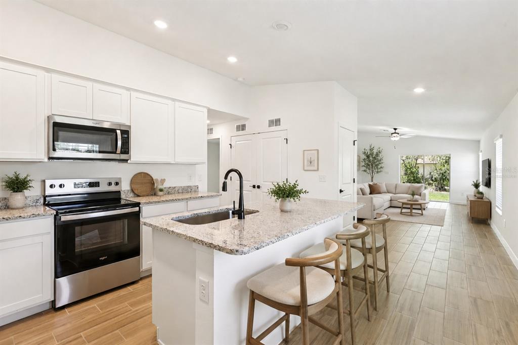 A modern kitchen with white cabinets, granite countertops, and an island with bar seating — 597 BLACKTHORN DRIVE, LAKELAND, FL