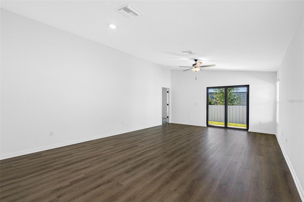 A spacious, empty living room features white walls, dark wood-look flooring, and sliding glass doors — 597 BLACKTHORN DRIVE, LAKELAND, FL