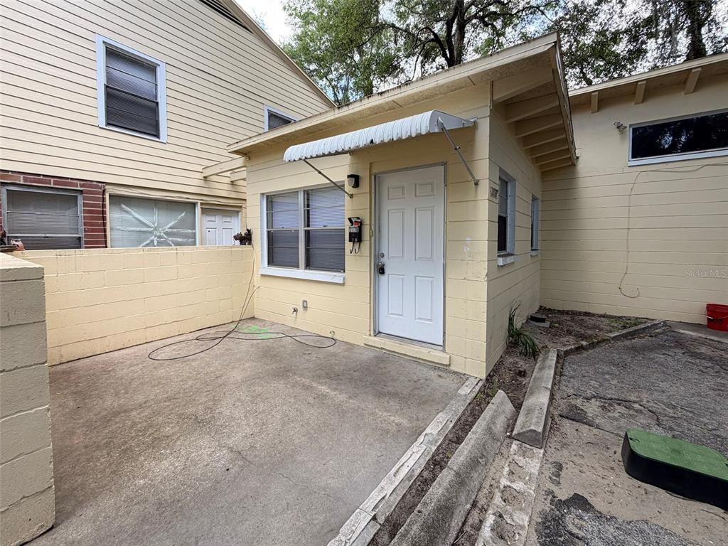 A small, yellow, single-story building with a white door and metal awning sits outdoors — 219 NW 3RD AVENUE UNIT B, GAINESVILLE, FL