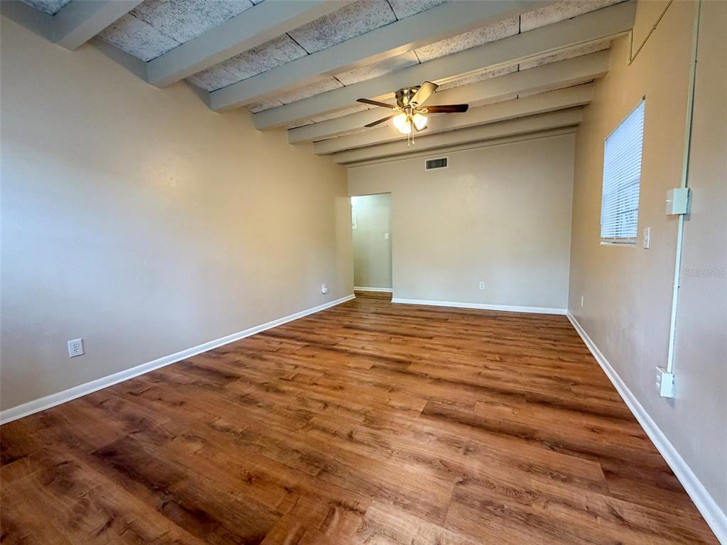 An empty room features wood-look flooring, exposed ceiling beams, and a ceiling fan — 219 NW 3RD AVENUE UNIT B, GAINESVILLE, FL