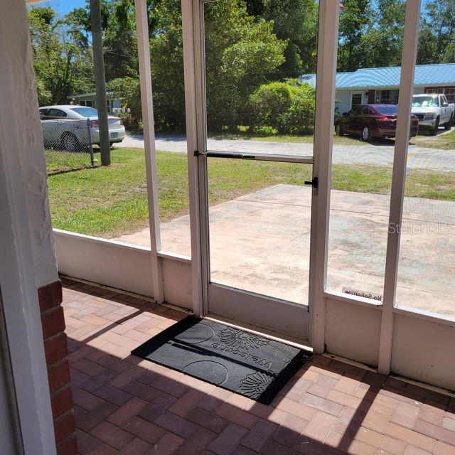 A screened-in porch with a brick floor, a welcome mat, and a view of parked cars — 7431 SHEEPSHEAD DRIVE, HUDSON, FL