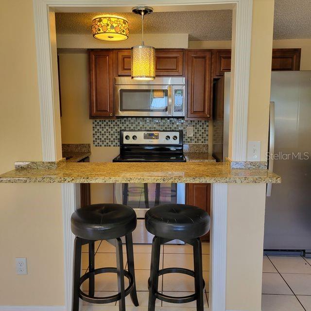 A kitchen with wood cabinets, granite countertops, and a breakfast bar with two black stools — 7431 SHEEPSHEAD DRIVE, HUDSON, FL